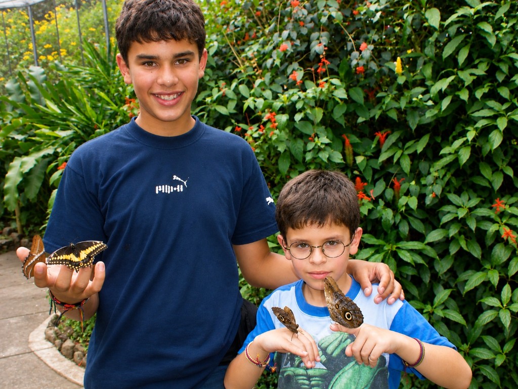 Juanes y Danny con mariposas posadas en las manos, en el mariposario