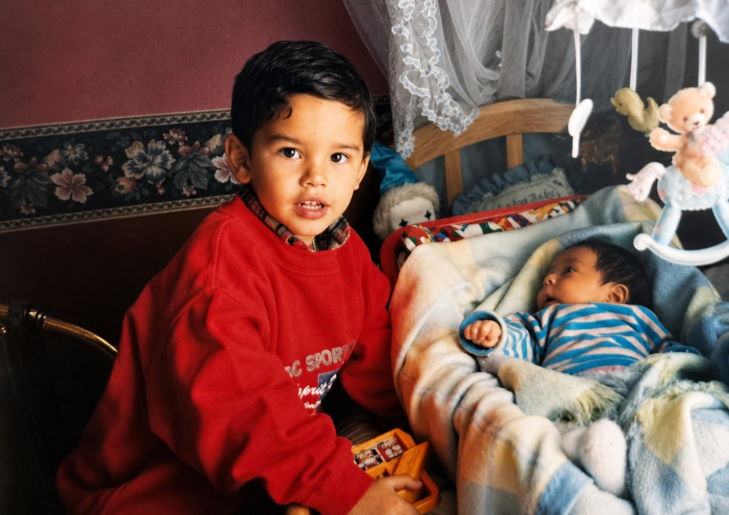 Juanes, de unos tres o cuatro años, de pie junto a la cuna donde duerme su hermano recién nacido
