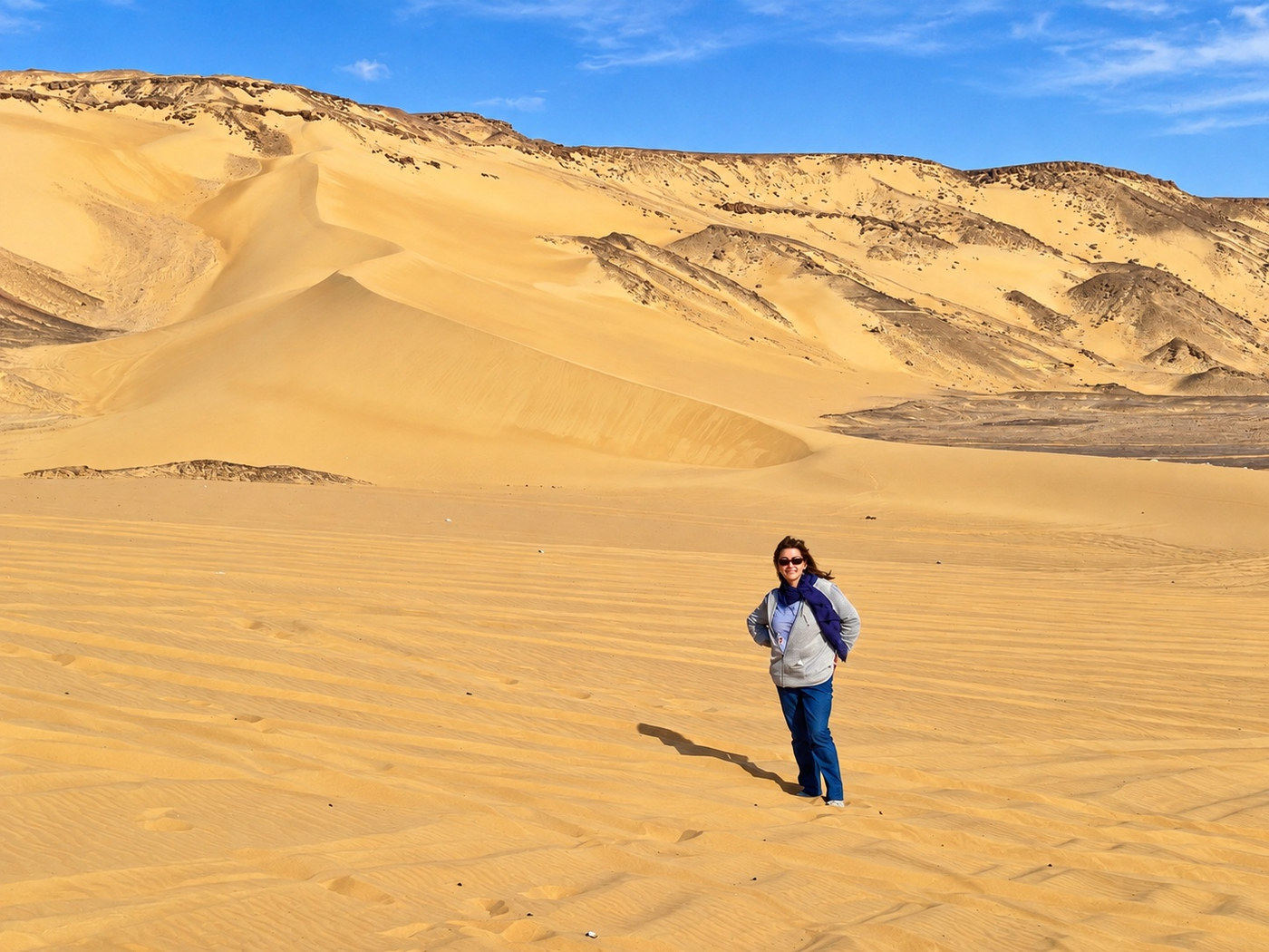 Alexandra sonríe en las dunas doradas del Sáhara, con colinas oscuras al fondo